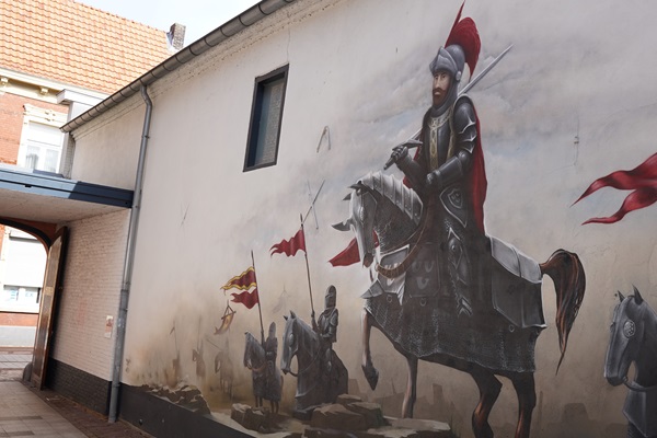 Een grote muurschildering van een middeleeuwse ridder in harnas op een paard, omringd door andere ridders met vlaggen, te zien langs de Street Art Route in Weert.