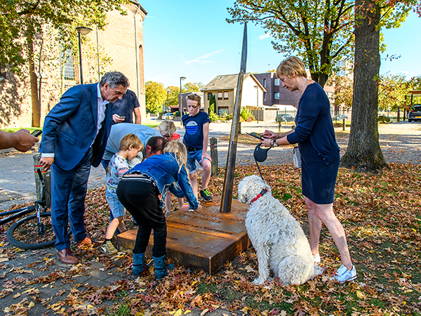 Een groep met volwassenen en kinderen doen de Archeo Route en staan bij een speer