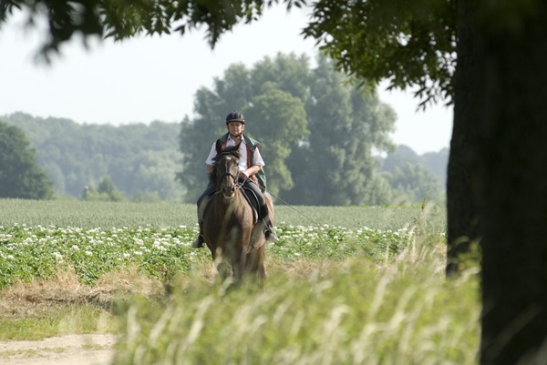 Reiter auf einem ländlichen Weg, umgeben von grünen Feldern und Bäumen im Naturschutzgebiet Leudal.