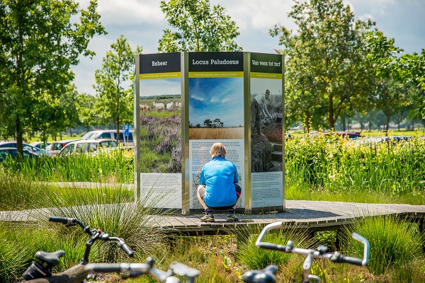 Mann schaut auf die Informationstafel am Buitencentrum De Pelen mit seinem Fahrrad im Vordergrund