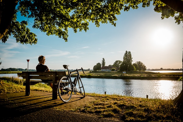Cyclist rests on a bench by the Meuse River and enjoys the sunset in Stevensweert