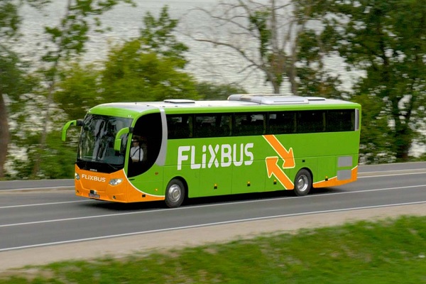 De groen-oranje Flixbus rijdt over de openbare weg langs een meer.
