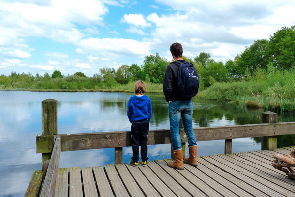 Man en kind staan op een houten vlonder en kijken naar het water