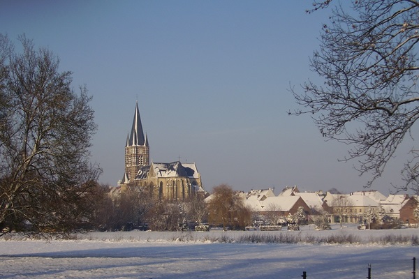 Winter view of the abbey church in Thorn, with snow-covered roofs and a white landscape in the foreground.