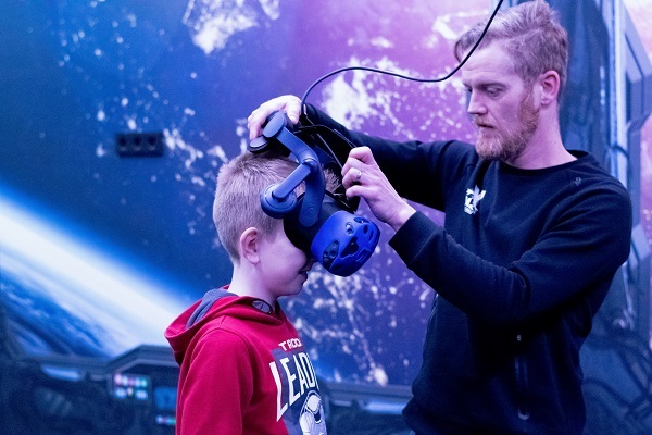 Medewerker helpt jongen met het opzetten van zijn VR bril. 