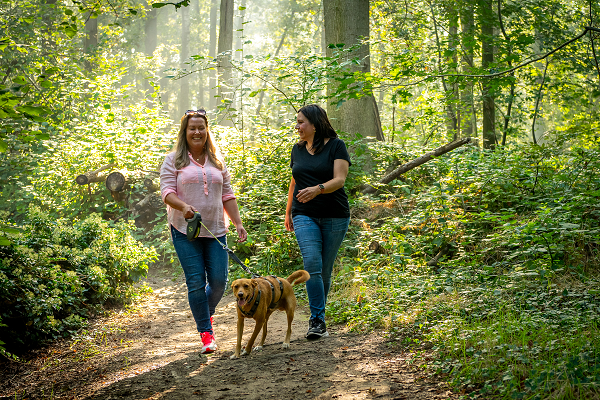 zwei Frauen gehen mit dem Hund durch die Natur