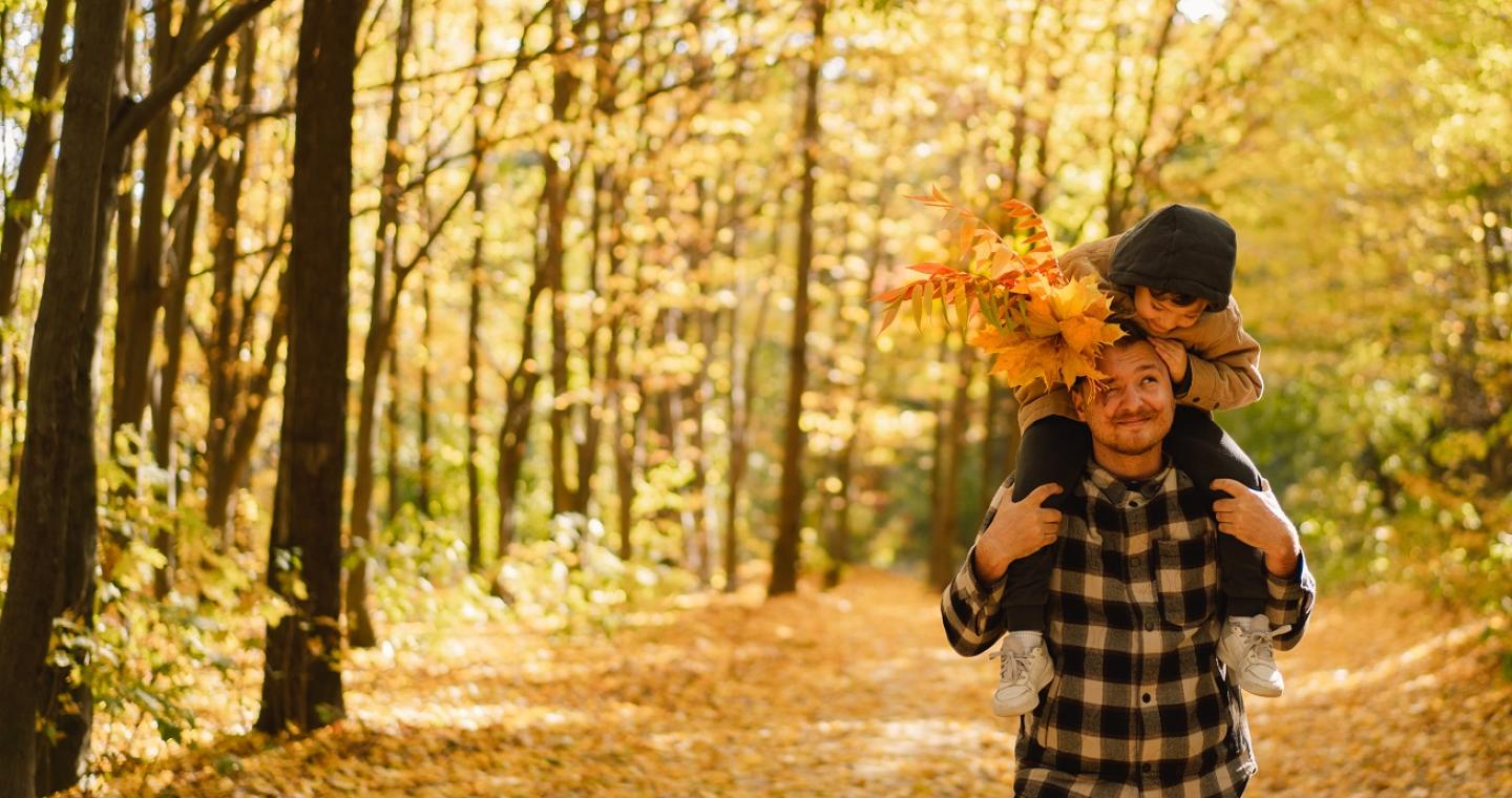 Zoon zit bij vader op de nek terwijl ze door een bos wandelen in de herfst