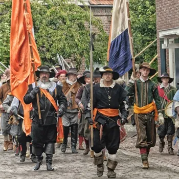 Historische optocht tijdens de Slag om Stevensweert, met deelnemers in 17e-eeuwse kleding die door de straat marcheren met vlaggen en wapens.