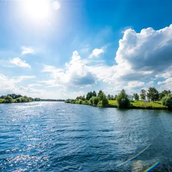 Zonnige zomerdag aan de Maasplassen met blauwe lucht, witte wolken en glinsterend water omringd door groen landschap.
