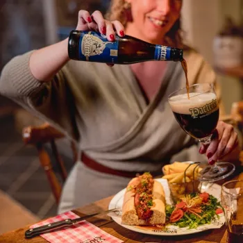 Vrouw schenkt een donker herfstbier in bij Boscafé De Busjop in Heythuysen, met op tafel een rijk gevulde lunchplank en warme sfeer in het restaurant.