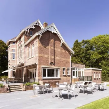 Statige bakstenen doktersvilla met terras en tuinmeubilair bij Villa Venray, omringd door groen en gelegen onder een heldere blauwe lucht.