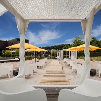 Loungegedeelte met witte stoelen, gele parasols en een houten looppad bij brasserie Boschmolenplas aan de Maasplassen.
