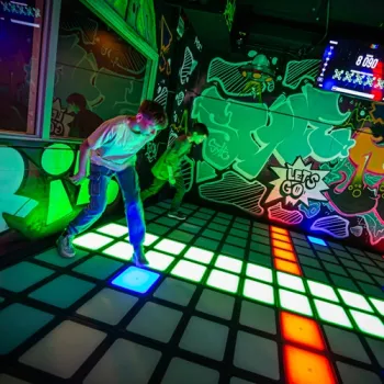 Twee jongeren spelen een interactief lichtspel op een kleurrijke vloer.