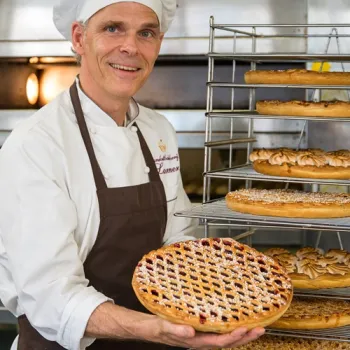 Vlaaibakker houdt een versgebakken Limburgse rastervlaai vast in de bakkerij.